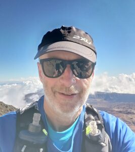 Clive Walker wearing sunglasses, running hat and with a blue sky background